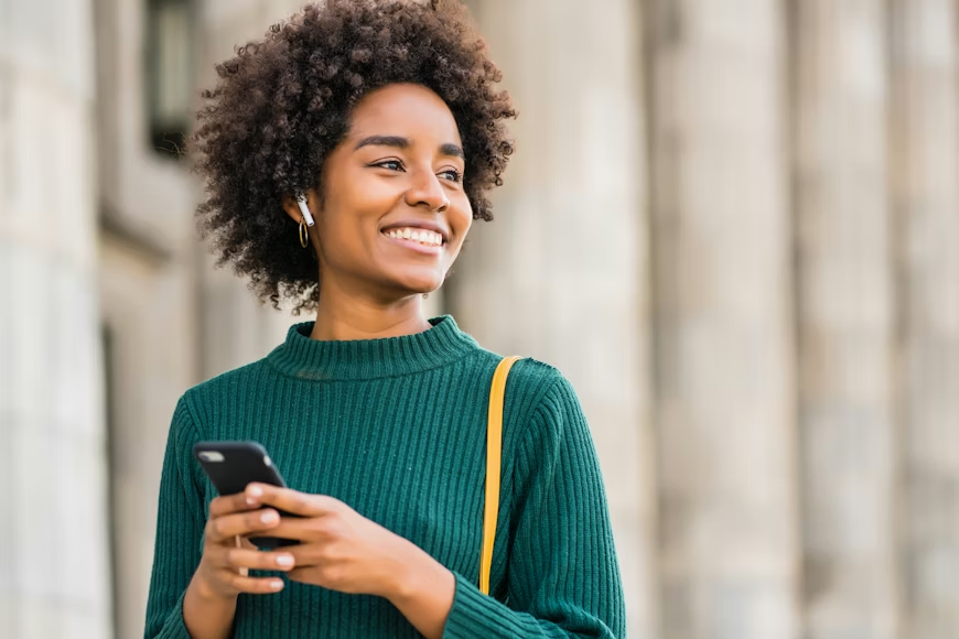 A happy young woman with an afro walking with a phone in her hands